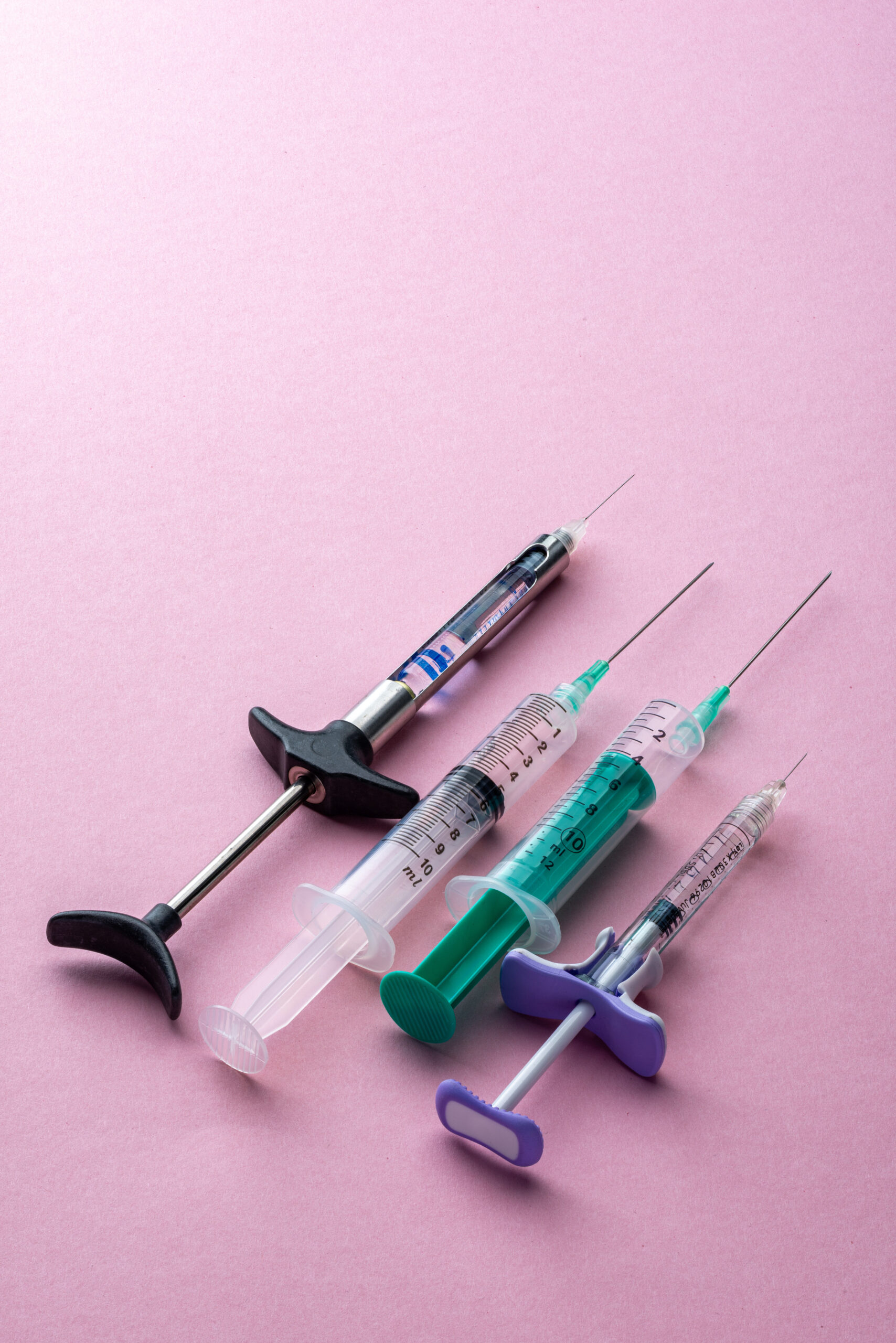 Four different kinds of Syringes, isolated on a pink background, high angle view, studio shot.